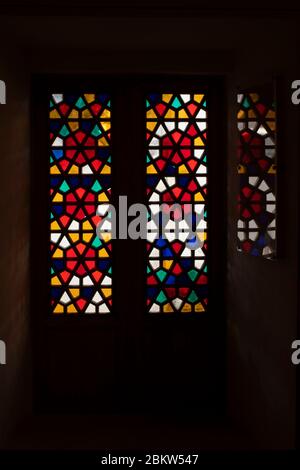 Eine Tür aus Buntglas-farbigem Glas. Das Muster spiegelt sich auf dem Glas. Das Foto ist dunkel und wirkt einschüchternd. Das Muster auf dem Buntglasfenster besteht aus vielen Fünfecken. Stockfoto