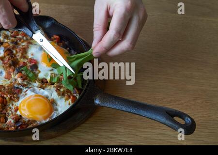 Food Hintergrund, Spiegeleier mit Gemüse in der Pfanne und männliche Hand mit Schere auf Holztisch, selektive Fokussierung Stockfoto