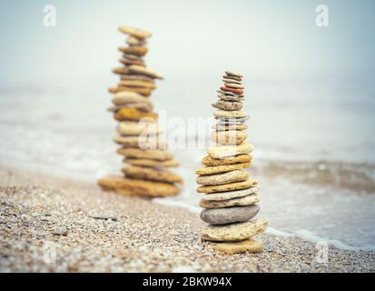 Steinpyramide auf Sand symbolisiert Zen, Harmonie, Gleichgewicht. Positive Energie. Ozean im Hintergrund Stockfoto