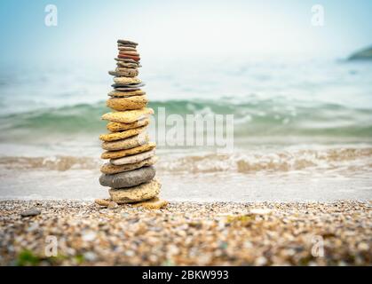 Steinpyramide auf Sand symbolisiert Zen, Harmonie, Gleichgewicht. Positive Energie. Ozean im Hintergrund Stockfoto