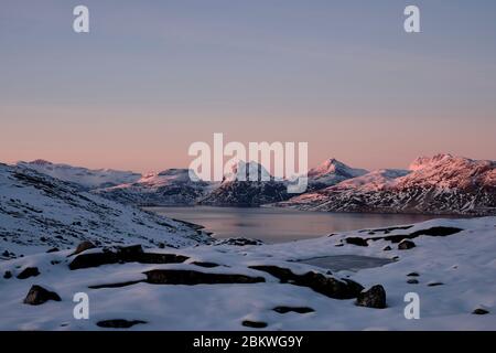 Lebhaft farbenprächtiger Sonnenuntergang über dem Wasser mit schneebedecktem Bergmassiv im Hintergrund. Stockfoto