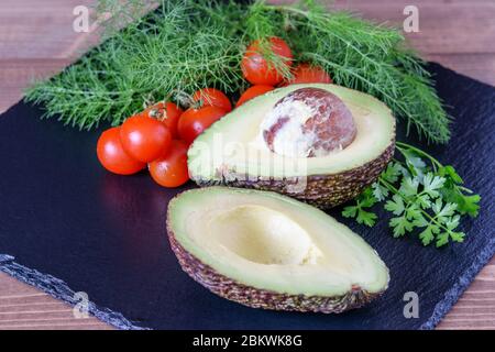 Hälften von frischen großen Avocado mit grünen Dill und Tomaten Kirsche auf der Küche schwarzen Brett. Vegetarische Ernährung Avocado Nahaufnahme. Stockfoto