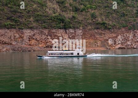 Wuchan, China - 7. Mai 2010: Dicui-Schlucht am Daning-Fluss. Weißes Fährschiff mit Passagieren, die auf smaragdgrünem Wasser vor dem braunen felsigen Gestein Rasen Stockfoto