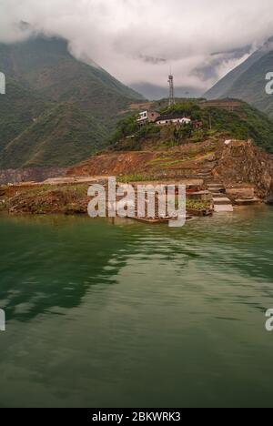 Wuchan, China - 7. Mai 2010: Dicui-Schlucht am Daning-Fluss. Porträt von Hügel mit landwirtschaftlichen Parzellen und weißen Bauernhof mit Antenne unter Wolkenlandschaft und em Stockfoto