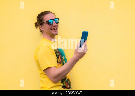 Lächelnder junger Mann mit Smartphone in Kontakt mit Familie und Freunden isoliert auf hellgelben Studio Hintergrund zu bekommen Stockfoto
