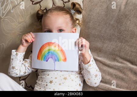 Kind Malerei Regenbogen während Covid-19 Quarantäne zu Hause. Mädchen mit einem Regenbogen. Bleiben Sie zu Hause Social Media Kampagne für Coronavirus, let's Stockfoto