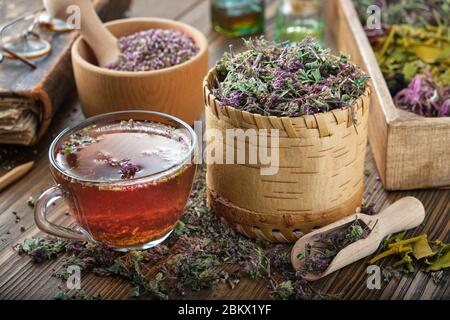 Tasse Tee mit wilden Marjoram und Erica Blumen. Trocken Origanum vulgare und Heidekraut Heilpflanzen, altes Buch und Flaschen ätherisches Öl auf Backgroun Stockfoto