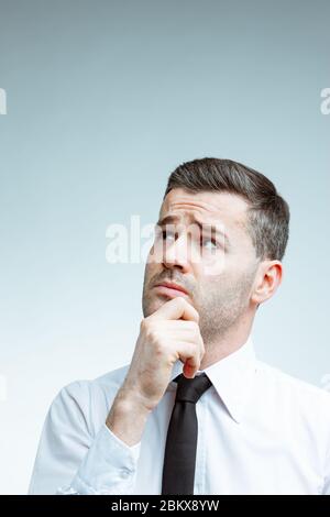 Nachdenklicher, schöner Mann mit akkurat angeschnittenem Haarschnitt, weißes Hemd mit schwarzem Krawatte, die Hand am Kinn haltend und aufblickend, an etwas denkend Stockfoto