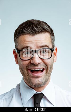 Verrückter lachender Geschäftsmann in einer Brille mit unrasierten Gesicht. Nahaufnahme des vorderen Porträts im Studio vor hellem, klarem Hintergrund Stockfoto