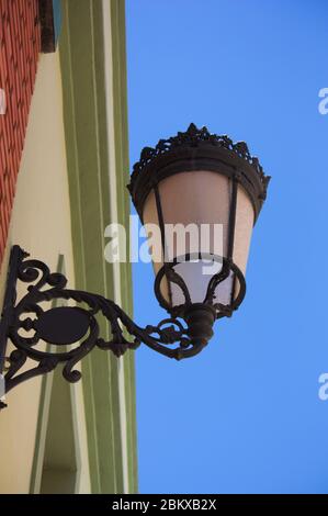 Nahaufnahme von unten eines alten Lampensteines, der an einer Wand befestigt ist, von wo aus er die Straße nachts beleuchtet Stockfoto