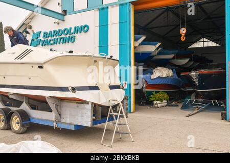 Mann, der Wartungsarbeiten auf einem Boot vor dem Bootshaus Bardolino Yachting am Ufer des Gardasees, Bardolino, Verona, Veneto, Italien durchführt Stockfoto