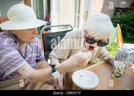 Ehemann und Ehefrau in ihren 90ern noch verliebt und die Frau hat Frühstadium Demenz Löffel gefüttert cake.Natural und nicht in ihrem Garten während Stockfoto