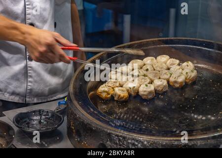 Chinesischer Koch kocht in der Küche gebratene Knödel auf einer heißen Pfanne Stockfoto