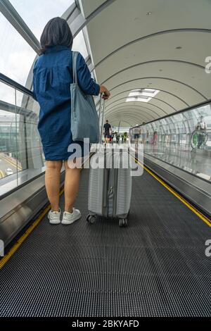 Junge Reisende mit Gepäck auf einem beweglichen Gang am Flughafen Stockfoto