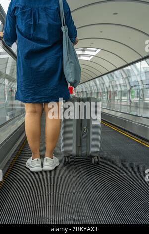 Reisende, die ihr Gepäck halten und auf einem automatischen Gehweg stehen Stockfoto