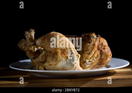 Hühnchen Abendessen aus nächster Nähe auf weißem Teller auf Holztisch serviert. Abendessen wird serviert gebratenes BBQ ganze Hühnchen isoliert auf schwarzem Hintergrund. Lecker keto mea Stockfoto