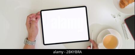 Ein Schuss Geschäftsmann, der mit einem leeren Tablet arbeitet und mit heißem Tee und Croissant frühstücken kann Stockfoto