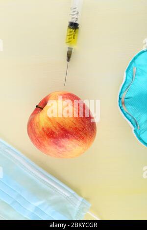 Chemische Zusatzstoffe in Lebensmitteln oder genetisch veränderte Frucht Konzept. Roter Apfel mit Spritzen von Chemikalien. Isoliert auf rotem Hintergrund. Stockfoto