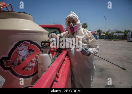 Tijuana, Mexiko. Mai 2020. Ein Mitglied der Gruppe "Covid Busters" steht in einem Schutzanzug neben dem Auto mit dem Logo der Gruppe am Rande einer Desinfektionskampagne gegen die Verbreitung von Covid-19 die Gruppe hat sich nach den US-Filmen "Ghostbusters" benannt und plant, Plätze in zu desinfizieren Die Stadt an der Grenze zu den USA, wo viele Menschen sich versammeln. Die Männer nehmen kein Geld für diese Arbeit. Es sind Bürger, Freunde und Familienväter, die diesen Dienst aus Liebe und Fürsorge für ihre Stadt tun, wie sie auf Facebook schreiben. Quelle: Omar Martínez/dpa/Alamy Live News Stockfoto