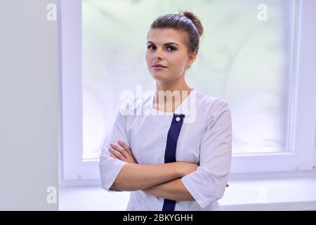 Porträt der jungen attraktiven selbstbewussten Frau in medizinischer Uniform mit gekreuzten Armen Stockfoto