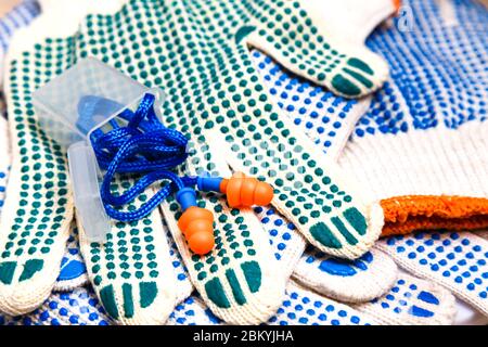 Dünne Arbeitshandschuhe mit grünen Noppen und Ohrenstöpseln aus nächster Nähe, Hintergrund der persönlichen Schutzausrüstung. Arbeitsschutzkonzept. Stockfoto