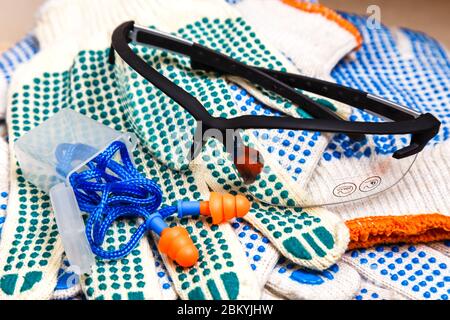Dünne Arbeitshandschuhe mit grünen Noppen, Schutzbrille und Ohrstöpsel aus nächster Nähe, Hintergrund der persönlichen Schutzausrüstung. Arbeitsschutzkonzept. Stockfoto