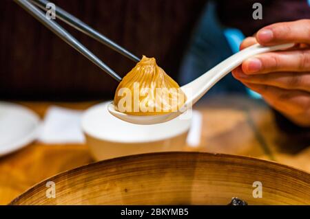 Eine chinesische Dame nimmt einen Foie Gras aromatisierten Gourmet xiaolongbao Suppenknödel mit Essstäbchen und einem Löffel. Stockfoto