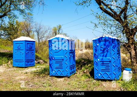 Drei blaue Kabinen von chemischen Toiletten in einem Park an sonnigen Sommertag. Stockfoto