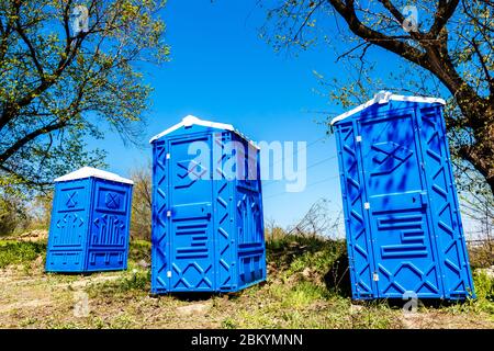 Drei blaue Kabinen von chemischen Toiletten in einem Park an sonnigen Sommertag. Stockfoto