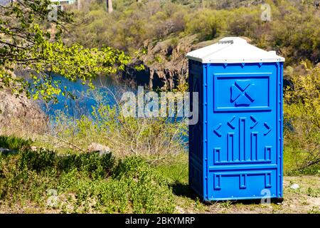 Blaue Kabine der chemischen Toilette in einem Bergpark auf einem Fluss Hintergrund an sonnigen Sommertag. Stockfoto