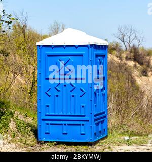 Blaue Kabine der chemischen Toilette in einem Bergpark an sonnigen Sommertag. Stockfoto