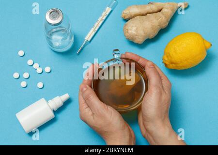 Nasenspray, Pillen, eine Glasflasche, ein Quecksilberthermometer, weibliche Hände mit einer Tasse Tee, Zitrone und Ingwer. Draufsicht. Konzept des Behandlungskits. Gesundheit Stockfoto