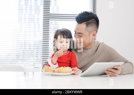 Junge asiatische Vater und Tochter essen Pizza beim Ansehen auf ipad. Stockfoto