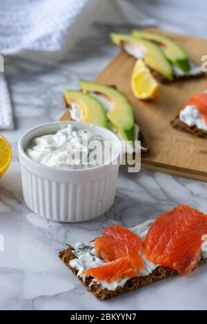 Frühstück am Morgen, zartes hausgemachtes Weichkäse auf Crackern mit geräucherter Forelle und Avocado Stockfoto