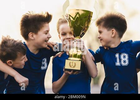 Happy Kids in Sports Team feiert Erfolg in Schulturnier. Junge Kaukasische Jungen Holding Golden Trophy. Kinder in Jugend Fußball-Team gewinnen Stockfoto