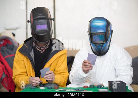 Zwei Schweißer in Schweißmasken spielen Poker Stockfoto