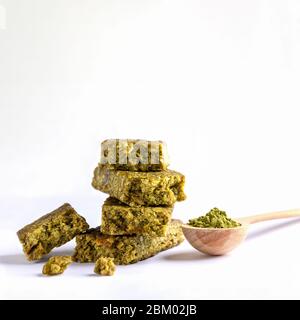 Stücke von Granola Bar im Stapel gefaltet und Holzlöffel mit Matcha grünen Tee Pulver auf weißem Hintergrund. Müsliriegel mit Matcha - gesunde Snacks reich Stockfoto