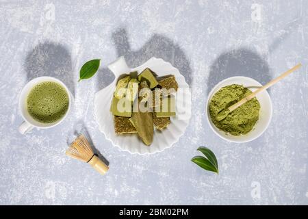 Matcha grüner Tee, Matcha Pulver, Leckereien mit Matcha, Schneebesen und Blättern auf hellgrauem Hintergrund mit Schatten. Matcha Tee und Desserts - gesund o Stockfoto
