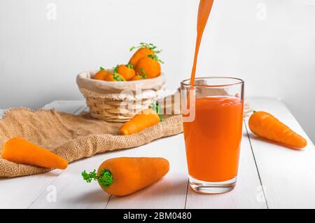 Karottensaft wird in ein transparentes Glas gegossen. Helle Sommerfotografie Stockfoto
