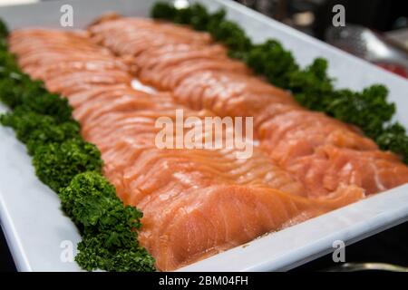 Frischer roher Lachs wird auf einem weißen Tablett mit Gemüsedekoration serviert. Stockfoto