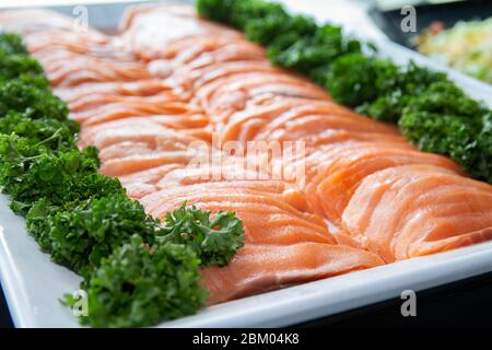Frischer roher Lachs wird auf einem weißen Tablett mit Gemüsedekoration serviert. Stockfoto