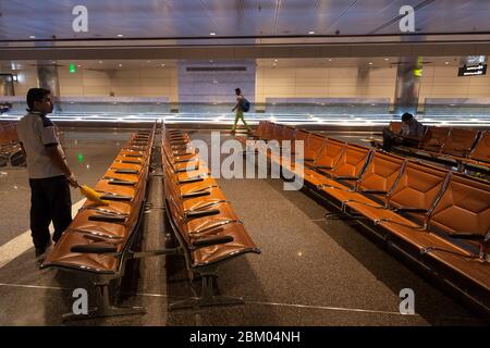 Ein südasiatischer Einwanderer reinigt Sitze für den Transfer von Passagieren innerhalb des internationalen Flughafens Hamad in Doha, Katar. Stockfoto