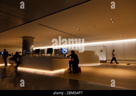 Ein südasiatischer Einwanderer putzt hinter Reisenden mithilfe von Computern an einem Internet-Service-Schalter im internationalen Flughafen Hamad in Doha, Katar. Stockfoto