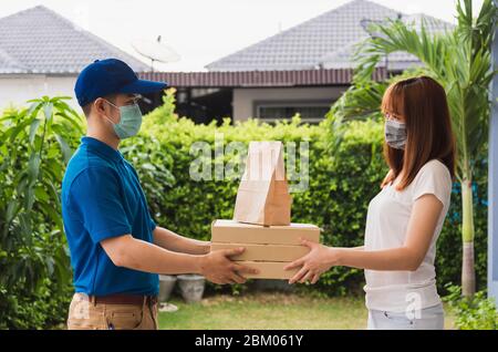 Asiatische Lieferung Express Kurier junger Mann geben Papiertüten Fast Food und Pizza-Box an Frau Kunde erhalten beide Schutzmaske Gesicht, unter Ausgangssperre Stockfoto