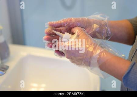Frau, die eine Flasche Haarfarbe in einem Badezimmer mischt, während sie sich darauf vorbereitet, mit Handschuhen in Nahaufnahme Farbe auf ihr Haar zu bringen Stockfoto