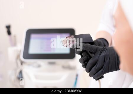 Nahaufnahme einer nicht erkennbaren Kosmetikerin in schwarzen Latexhandschuhen, die auf den Griff der Gesichtsmaschine zeigt und dem Kunden erklärt, wie sie funktioniert Stockfoto