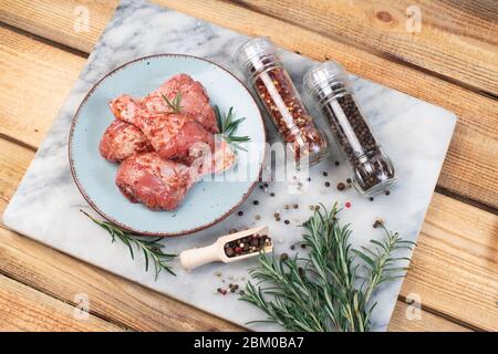 Kochen Hähnchenschenkel in roter Marinade . Rohe Hähnchenbeine in einer Marinade mit Rosmarin und Pfeffer auf einem marmornen Küchenbrett auf Holzhintergrund. Stockfoto