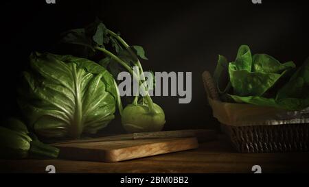 Nahaufnahme von frischem grünem Gemüse Kohlrabi Rübenkohl und Zucchini auf Holztisch und Holzhackbrett in Low-Light-Fotografie Stockfoto