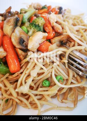 Pasta mit Gemüse, Pilzen und Huhn auf einem weißen Teller. Chinesische Nudeln, gebratenen Soba Nudeln mit Champignons, Möhren, Paprika closeup auf weißen Plat Stockfoto