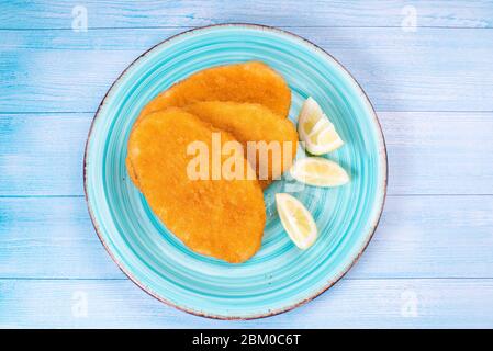 Panierte Hühnchen Schnitzel auf einem blauen Teller mit Zitronenscheiben auf blauem Holzhintergrund.Draufsicht, flacher Einschnitt Stockfoto